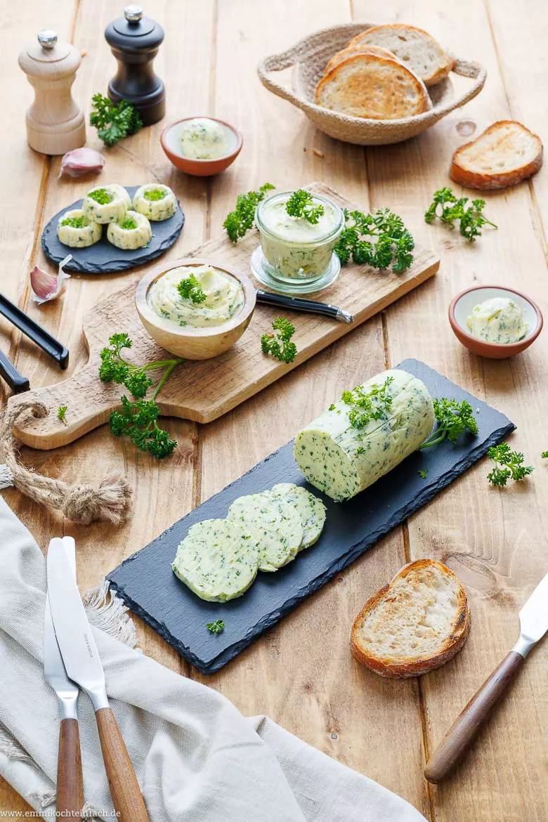 Kräuterbutter in verschiedenen Anrichteformen von Rolle über Kugel bis Mini-Gugelhupf sowie frisch geröstetes Brot