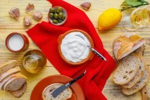 In einem Terrakotta-Schälchen selbst gemachte Aioli ohne Ei, drum herum die dafür verwendeten Zutaten: Knoblauch, Olivenöl, Zitronensaft und Milch