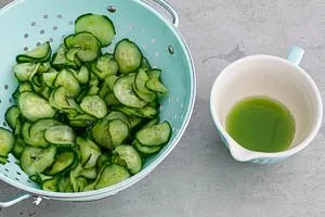 Entwässerte Gurkenscheiben im Sieb und eine Tasse mit Gurkenwasser