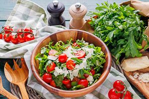 Fertig zubereiteter Rucola-Salat mit Kirschtomaten und Parmesanspänen in einer Holzschale