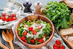Rucola-Salat mit Kirschtomaten und gehobeltem Parmesan in einer Holzschale frisch servieren