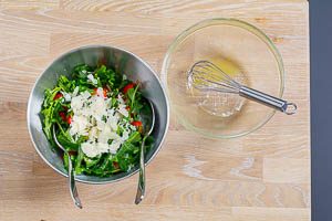 Alle Zutaten und Dressing für Rucola-Salat in einer Schüssel miteinander vermischt