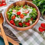 Salatschüssel aus Holz gefüllt mit Rucola-Salat mit Kirschtomaten und Parmesan