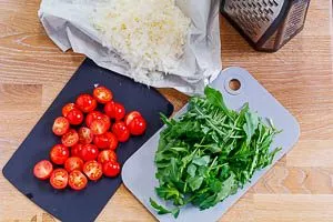 Gehobelter Parmesan, halbierte Kirschtomaten und klein geschnittener Rucola für Spaghettisalat