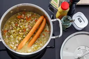 Abschmecken und Wiener Würstchen zur Erbensuppe geben