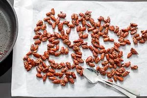 Breite die gebrannten Mandeln noch warm auf Backpapier aus, damit sie nicht aneinander kleben