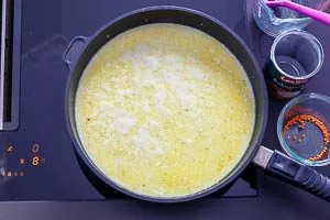 Gemüsebrühe, Kokosmilch, rote Linsen und gelbe Currypaste in die Pfanne geben