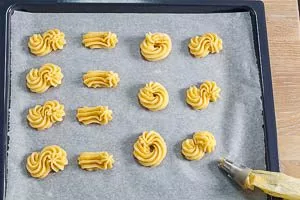 Spritzgebäck auf das Backpapier spritzen und im vorgeheizten Backofen backen.