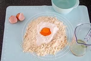 Aus dem Mehl, Zucker und Mandeln eine Mulde formen und Eigelbe hineingeben.