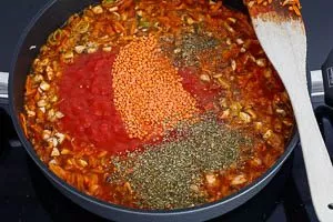 Rote Linsen und Gemüsebrühe zum Gemüse in die Pfanne