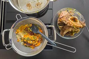 Ausgekochtes Gemüse und Fleisch durch Abgießen von der klaren Brühe trennen