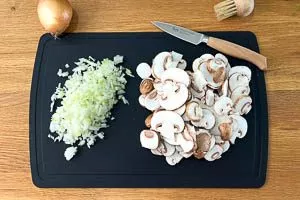 Zwiebeln und Champignons klein schnippeln.