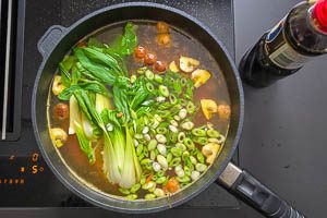 Mit Rinderbrühe aufgießen, Pak Choi, Frühlingszwiebeln und Sojasoße zugeben.