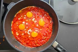 Eier in die Mulden im Shakshuka geben