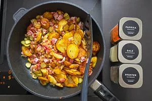 Bratkartoffeln, Zwiebeln, Speck, Cornichons und Gewürze vermengen