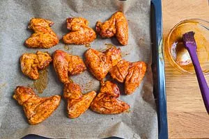 Chicken Wings mit der Marinade ummanteln und im Ofen backen.