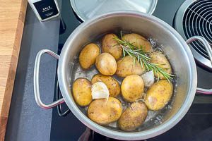 Kartoffeln im Kochtopf miot Salzwasser, Knoblauchzehen und Rosmarin kochen