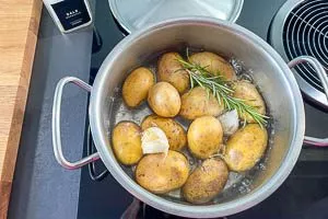 Kartoffeln im Kochtopf miot Salzwasser, Knoblauchzehen und Rosmarin kochen