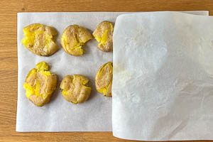 Gekochte Kartoffeln auf dem Backpapier zerdrücken