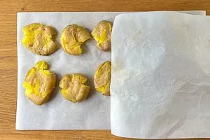 Gekochte Kartoffeln auf dem Backpapier zerdrücken