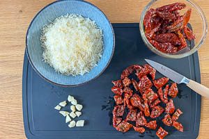 Parmesan, Knoblauchzehen und getrocknete Tomaten vorbereiten.