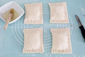 Die geschlossenen Taschen aus Blätterteig vorsichtig einritzen und mit Eiweiß bestreichen