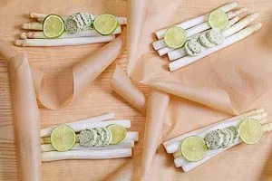 Zucker, Salz, Kräuterbutter und Limetten auf dem Spargel verteilen und auf das Backpapier legen.