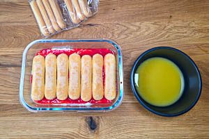Weitere in Orangensaft getränkte Löffelbiskuits auf die vorherigen Schichten verteilen