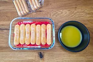 Weitere in Orangensaft getränkte Löffelbiskuits auf die vorherigen Schichten verteilen