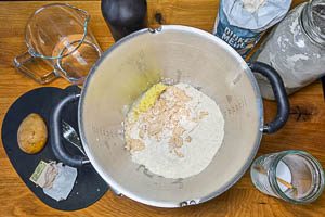 Wasser, Dinkelmehl und Weizenmehl, Öl, Salz, frische Hefe und die zerquetschten Kartoffeln mit dem Vorteig vermengen.