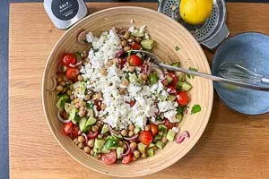 Kichererbsen, Zwiebeln, Gurke, Kirschtomaten und Kräuter mit dem Dressing vermischen