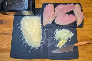 Zwiebeln und Knoblauch klein schneiden, Parmesan fein reiben und die Hähnchenbrustfilets der länge nach halbieren.