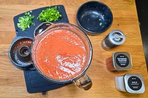 Paprika, Gurke, Frühlingszwiebeln und Knoblauch dazugeben und erneut pürieren. Eingeweichtes Brötchen und Gewürze dazugeben und alles zerkleinern.