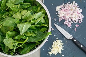 Weitere Zutaten für gefüllte Champignons vorbereiten: Spinat, Zwiebeln und Knoblauch.