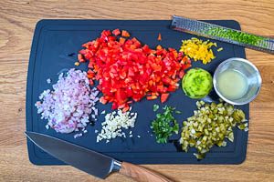 Die Zutaten für deine Salsa fein würfeln und sie auf einem Schneidebrett anrichten. Limette auspressen und die Schale abreiben.