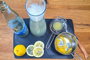 Sirup ohne die Zitronenschalen, Zitronensaft, Mineralwasser und Zitronenscheiben in einer Karaffe vermischen.