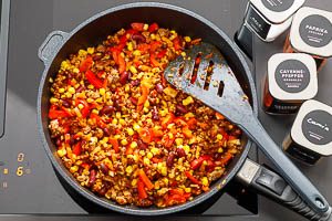Würze das Hackfleisch und gib die Zwiebeln, den Knoblauch, die Paprika, den Mais und die Kidneybohnen ebenfalls in die Pfanne.