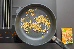 Röste die Pinienkerne in einer Pfanne an.