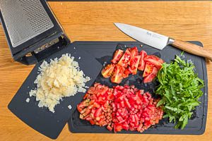 Wasche die Tomaten und schneide sie in kleine Würfel. Säubere den Rucola und zupfe ihn in kleine Stücke und reibe den Parmesan.