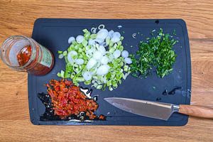 Schneide die Petersilie, die Frühlingszwiebeln und die halbgetrockneten Tomaten.