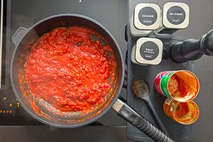 Stückige Tomaten, Ajvar und Gewürze in die Pfanne geben