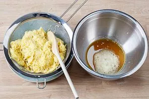 Flüssigkeit durch ein Sieb aus den geriebenen Kartoffeln drücken