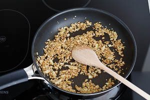 Kreuzkümmel, Chiliflocken, Sesam und Zwiebel in einer Pfanne anbraten
