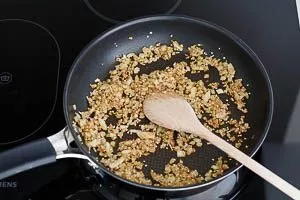 Kreuzkümmel, Chiliflocken, Sesam und Zwiebel in einer Pfanne anbraten
