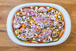 Kritharaki-Auflauf mit Zwiebelringen und Feta toppen