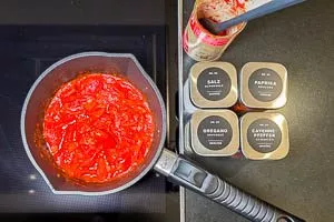 Mit ganzen Tomaten aus der Dose ablöschen und würzen. Köcheln lassen und die Zutaten mit einem Kochlöffel leicht zerdrücken