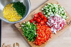 Schneide die Salatgurke, Paprika, Radieschen, Kirschtomaten, Frühlingszwiebeln und Schnittlauch klein. Gib das Gemüse anschließend mit dem Mais zum Dressing.