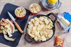 Backform einfetten und Äpfel schälen, schneiden und in die Auflaufform legen