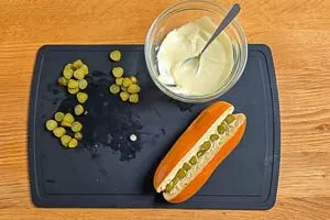 Hotdog-Brötchen mit der Soße und Gewürzgurken belegen