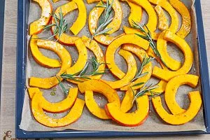 Hokkaidokürbis auf ein Backblech mit Backpapier verteilen und Rosmarin darauf geben. Dann in den vorgeheizten Backofen geben.